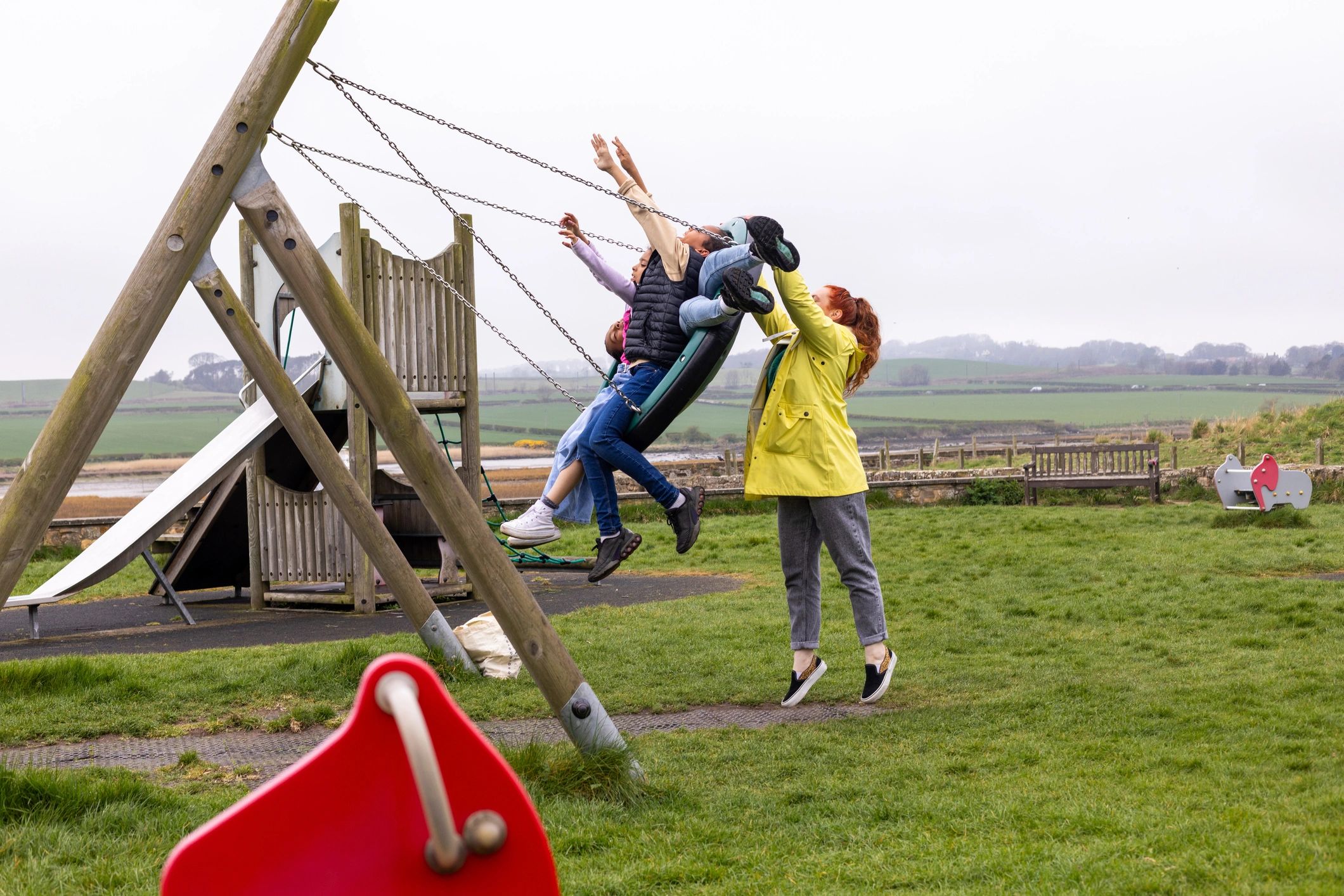 Children smiling on a basket swing while their mother pushes